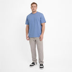 A man wearing a light blue Elements T-Shirt paired with light gray trousers and black shoes.