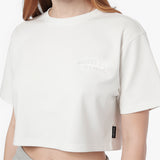 A cropped white T-shirt with a tonal 'JAMES BARK ELEMENTS' logo on the left chest and a small black brand tag on the lower hem, shown on a model.