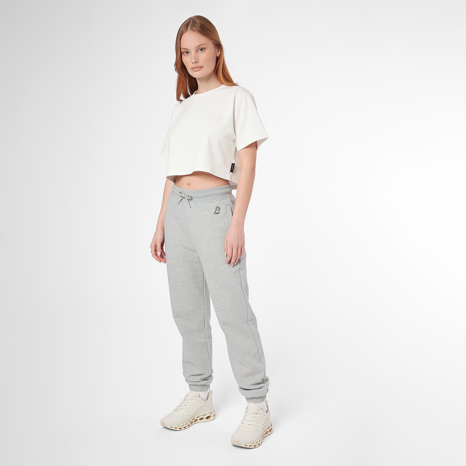 A woman modeling a white cropped T-shirt and light gray jogger sweatpants with white sneakers