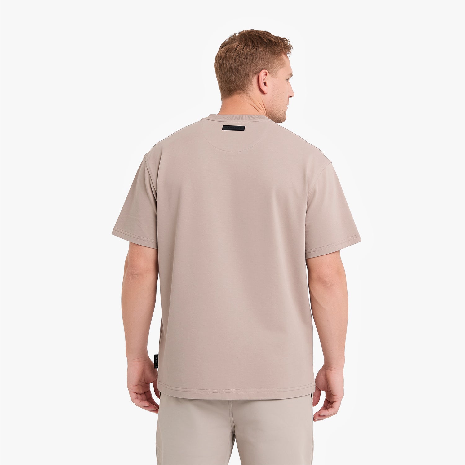 A man viewed from the back wearing a light beige short-sleeve t-shirt and matching beige pants