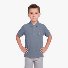 A young boy modeling a slate blue polo shirt with a small embroidered dog logo on the chest