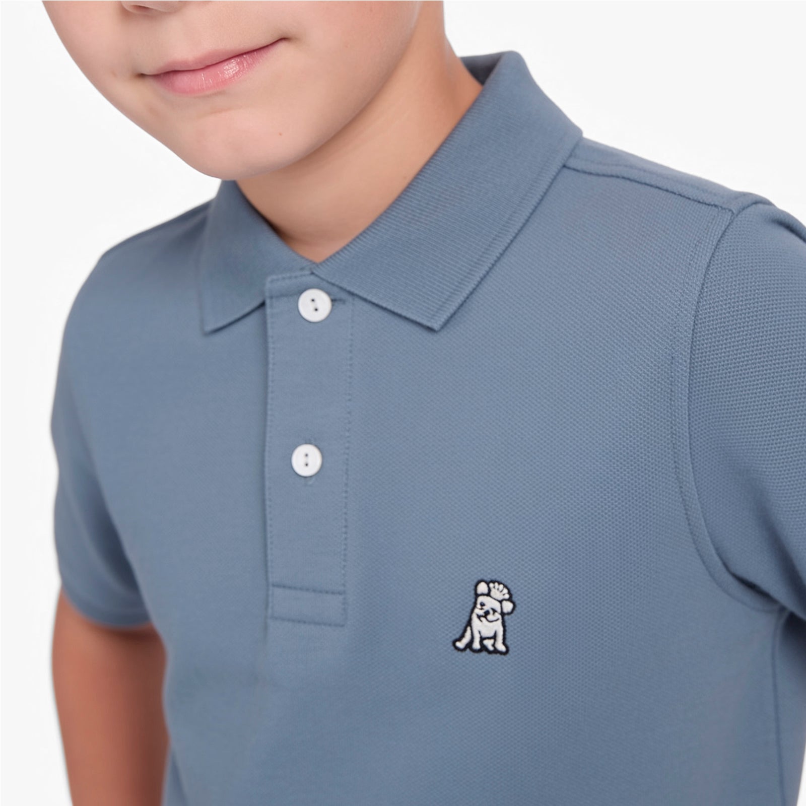 Close-up of a boy wearing a slate blue gray polo shirt with a white embroidered dog