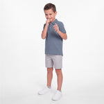 A young boy modeling a slate blue polo shirt, light gray shorts, and white sneakers