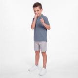 A young boy modeling a slate blue polo shirt, light gray shorts, and white sneakers