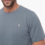 Gray t-shirt with a small logo on the chest worn by a person.
