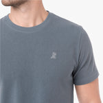 A close-up of a man wearing a gray crew-neck t-shirt with a small white embroidered dog logo