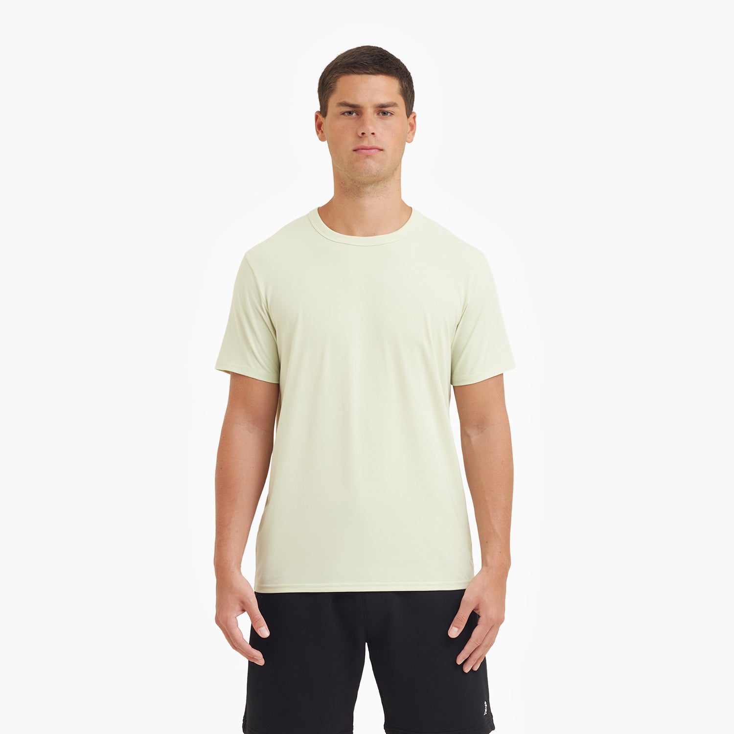 Man wearing a light green t-shirt and black shorts on a white background