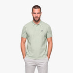 Man wearing a light green polo with a white embroidered logo on a white background