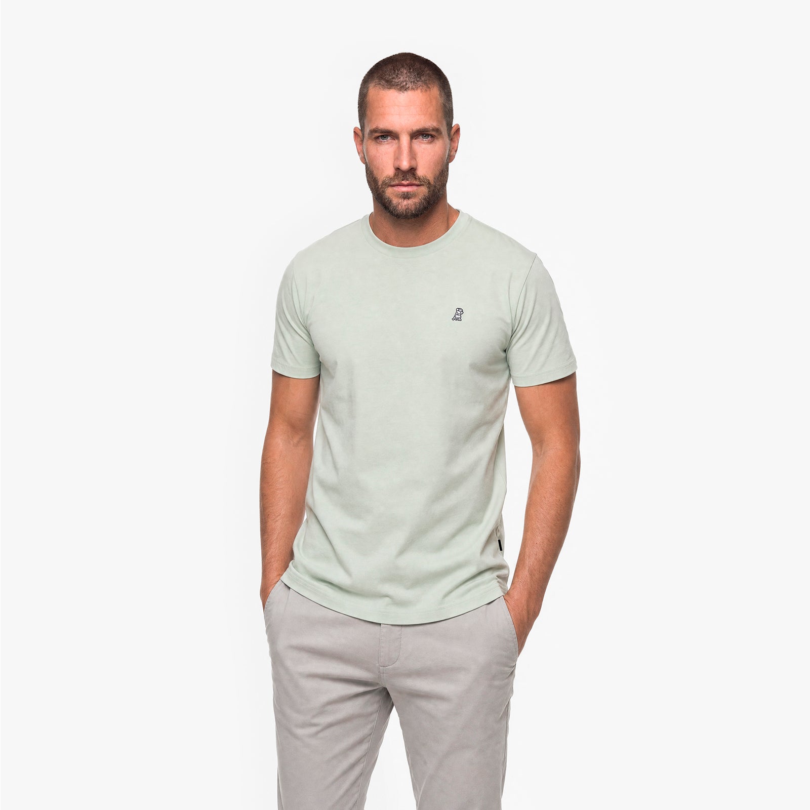 Man wearing a light green t-shirt and light gray pants on a white background