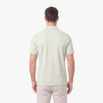 A man viewed from the back wearing a light sage green short-sleeve polo shirt and light beige trousers