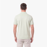A man viewed from the back wearing a light sage green short-sleeve polo shirt and light beige trousers