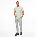 Man wearing a light green polo shirt and gray pants on a white background