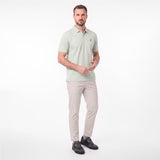 A man modeling a light sage green short-sleeve polo shirt with beige trousers