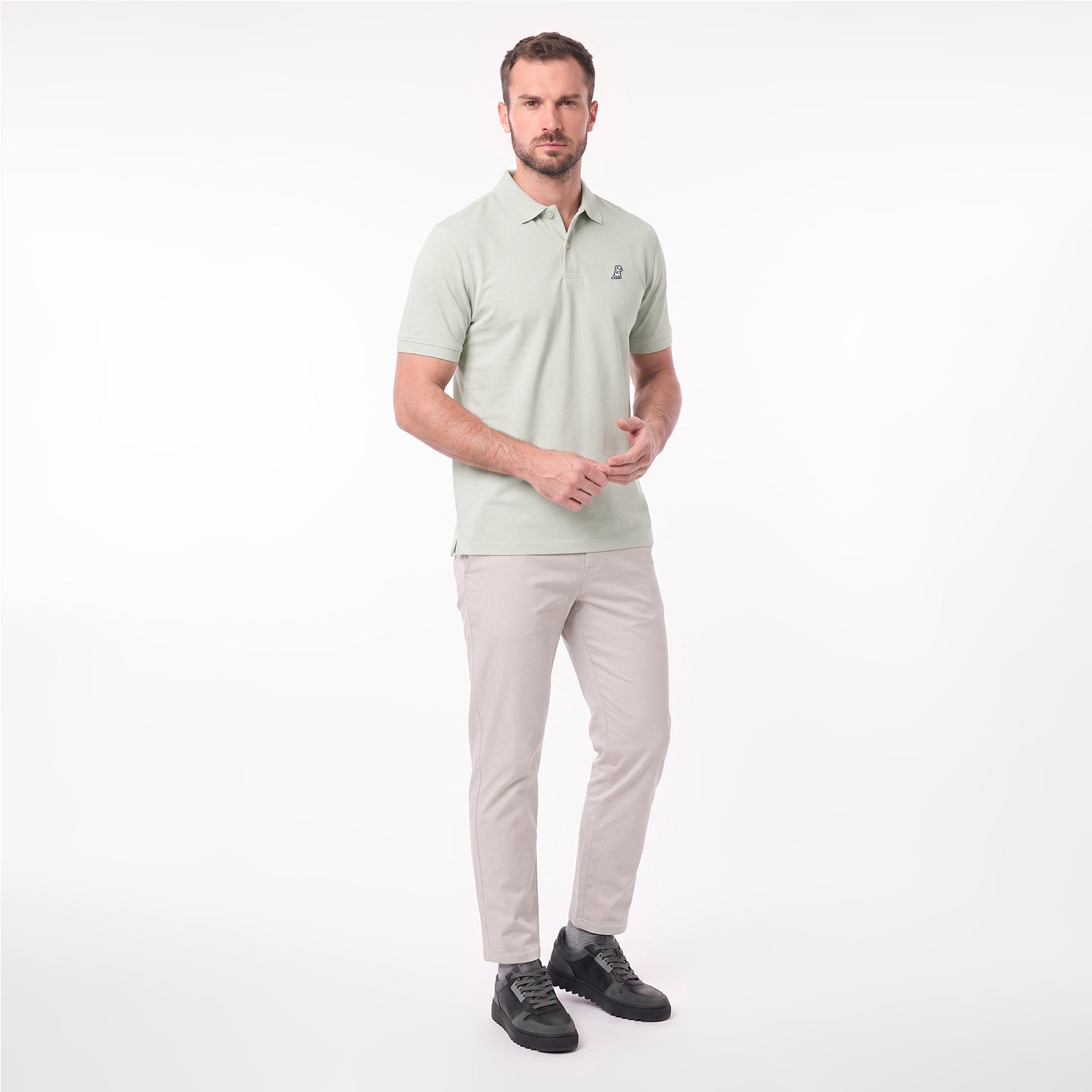 A man modeling a light sage green short-sleeve polo shirt with beige trousers