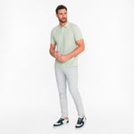 Man wearing a light green polo shirt and gray pants on a white background