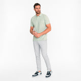Man wearing a light green polo shirt and gray pants on a white background