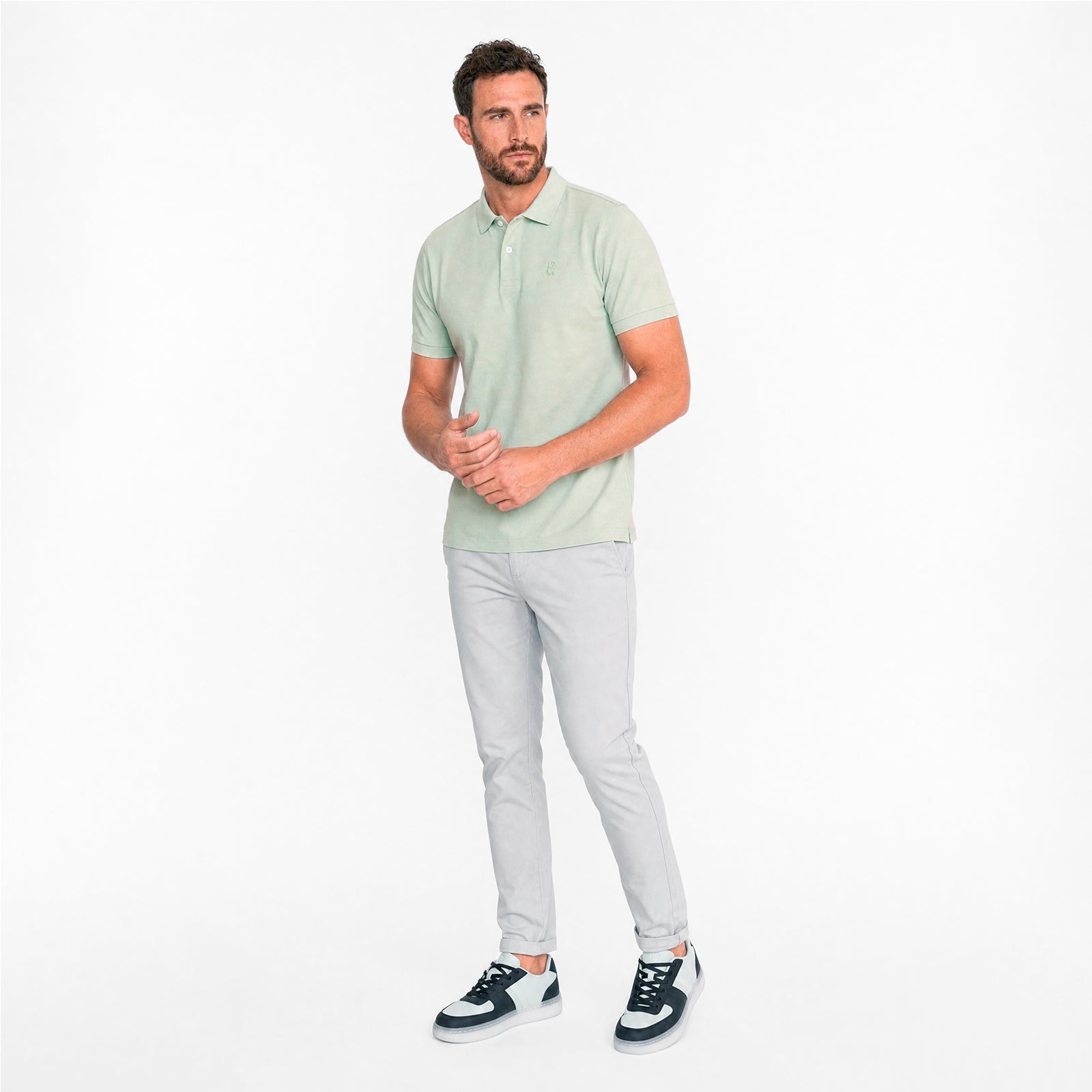 Man wearing a light green polo shirt and gray pants on a white background