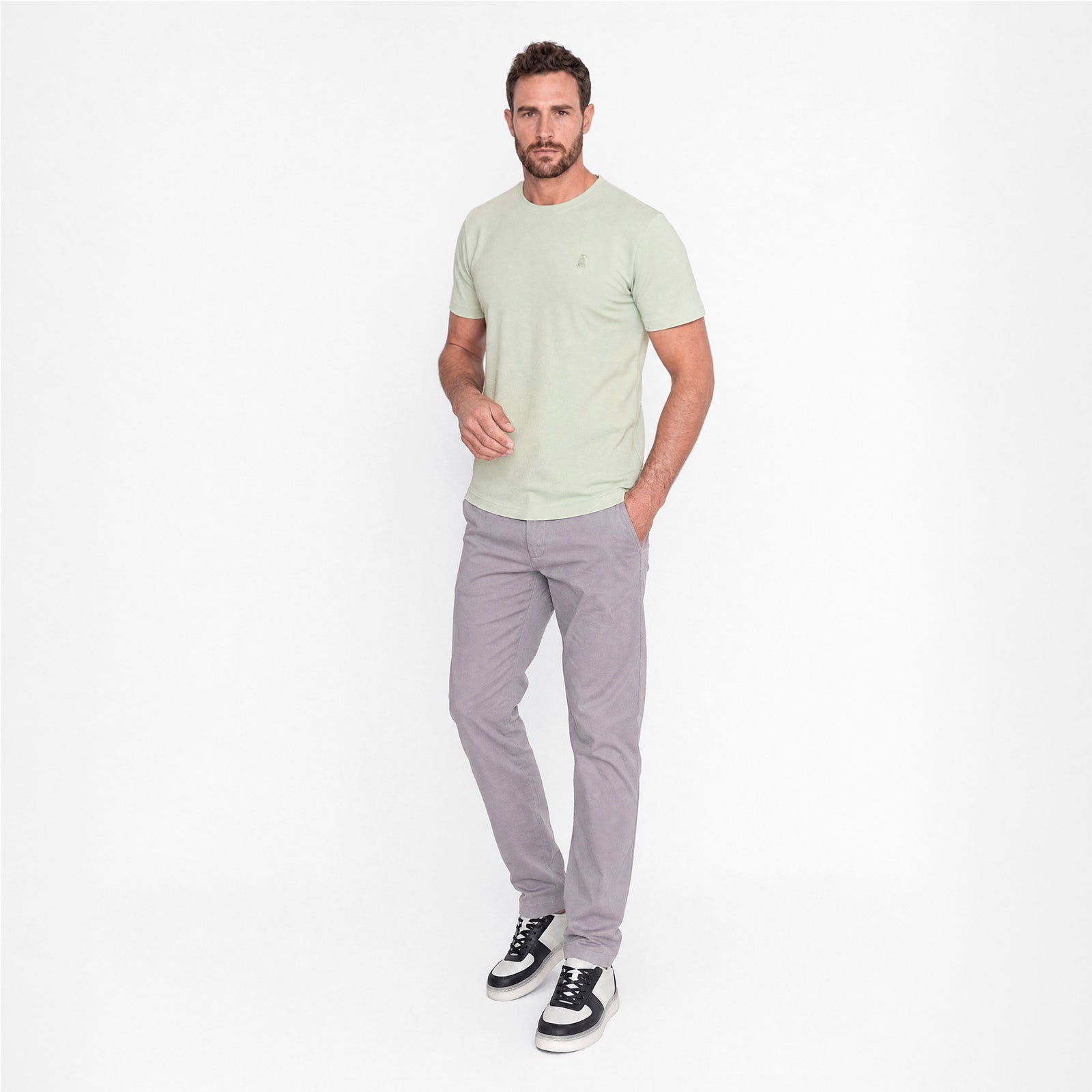 Man wearing a light green t-shirt and gray pants on a white background