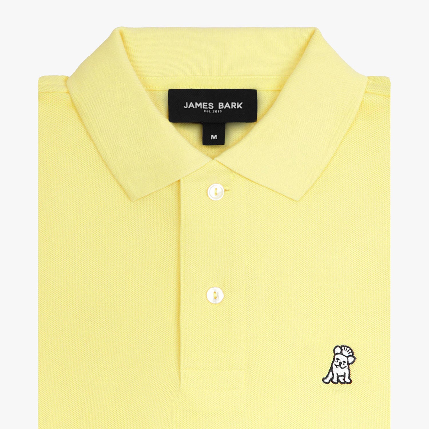 Close-up of the collar and tag of the light yellow polo shirt, focusing on the buttons and embroidered logo.