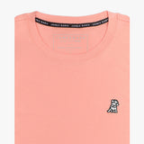 Close-up of the light pink t-shirt showing the crew neckline and a small embroidered animal logo on the left chest.