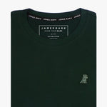 Close-up of the dark green t-shirt showing the crew neckline and a small embroidered animal logo on the left chest.