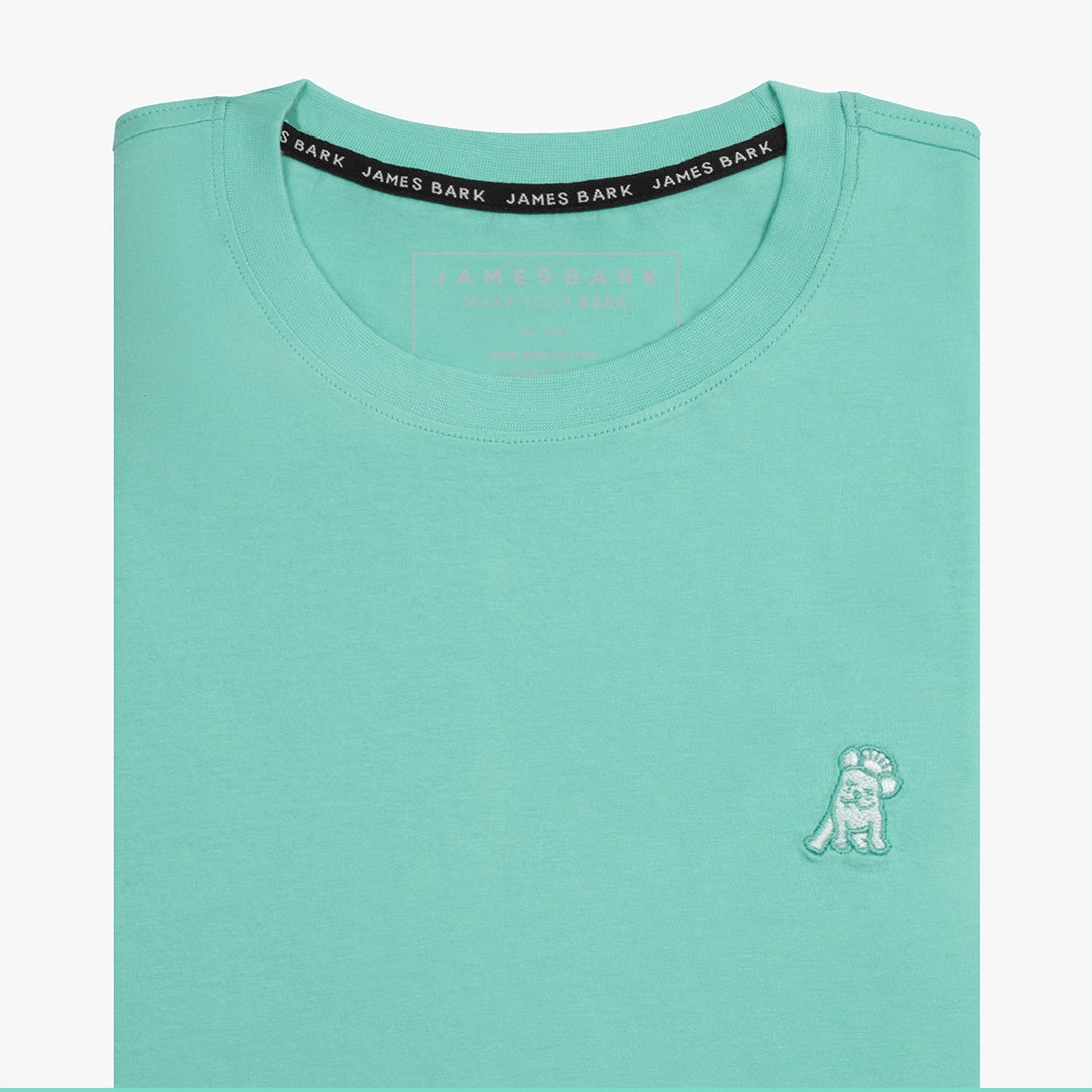 Close-up of the mint green t-shirt showing the crew neckline and a small embroidered animal logo on the left chest.