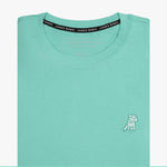 Close-up of the mint green t-shirt showing the crew neckline and a small embroidered animal logo on the left chest.