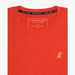 Close-up of the orange t-shirt showing the crew neckline and a small embroidered animal logo on the left chest.