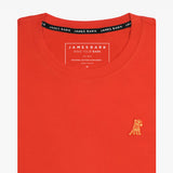 Close-up of the orange t-shirt showing the crew neckline and a small embroidered animal logo on the left chest.