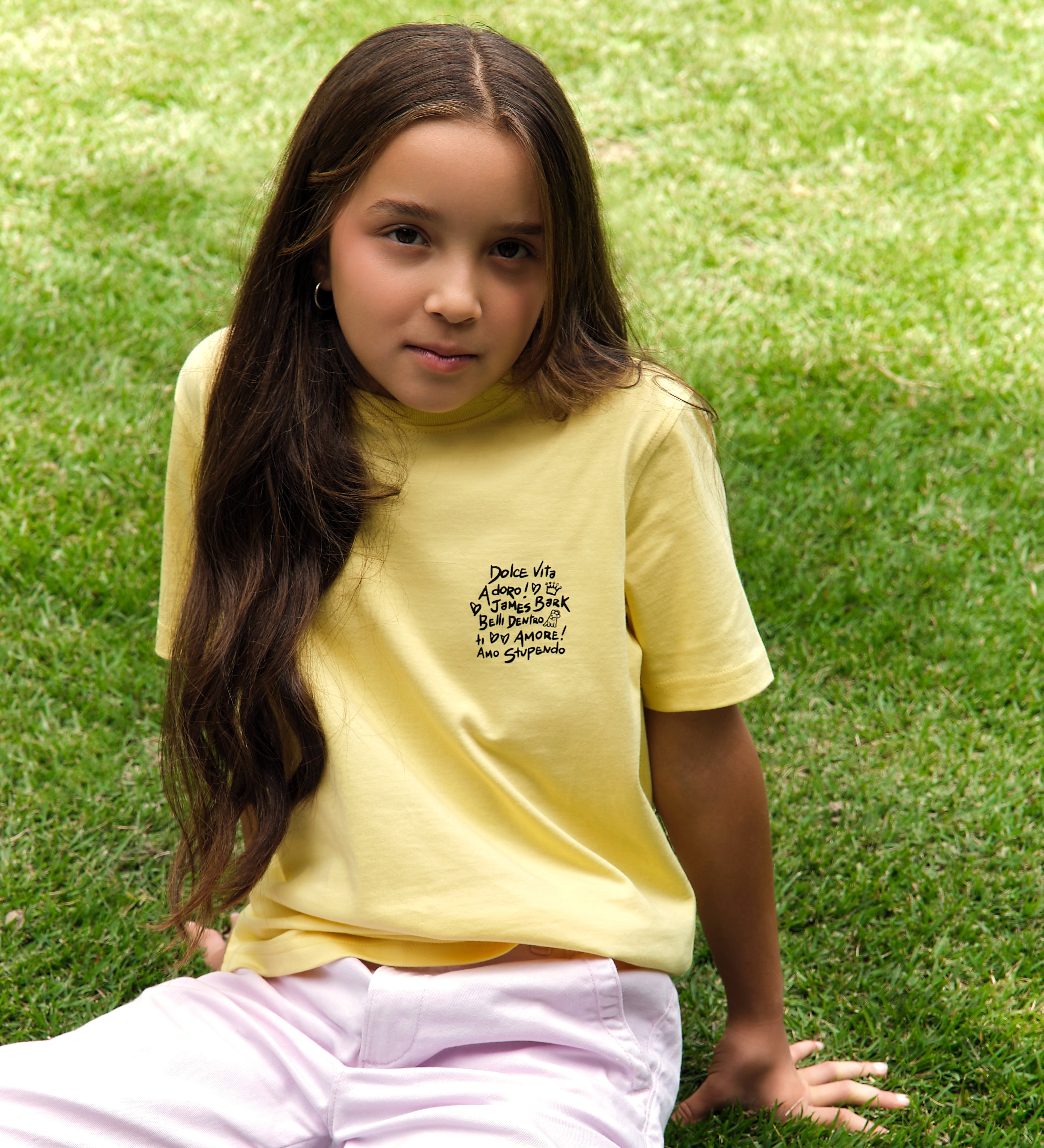 Young girl sitting on grass wearing a yellow t-shirt with text