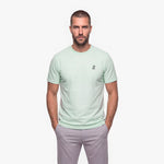Man wearing a light green t-shirt with a white embroidered logo on a white background