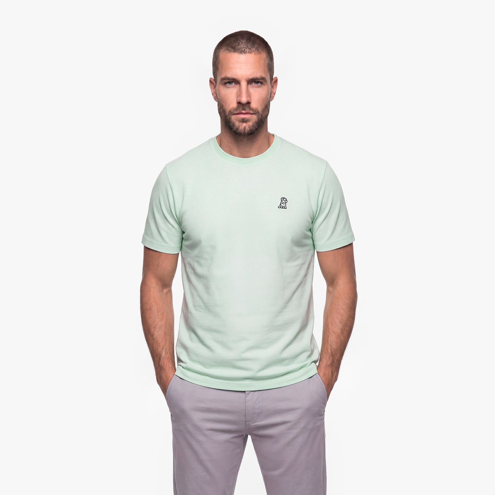 Man wearing a light green t-shirt with a white embroidered logo on a white background