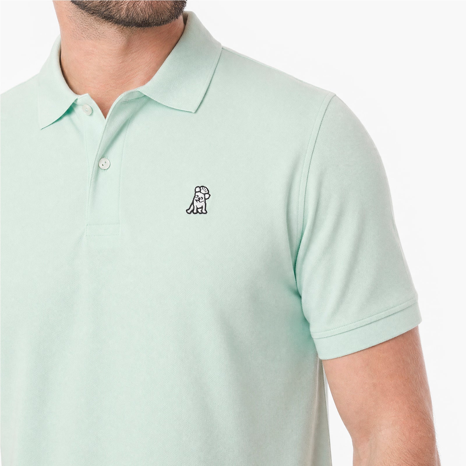 A close-up of a man wearing a light mint green polo shirt with a small embroidered dog logo on the chest