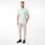 A man modeling a light mint green polo shirt with a small embroidered logo on the chest, paired with beige trousers
