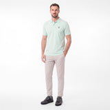 A man modeling a light mint green polo shirt with a small embroidered logo on the chest, paired with beige trousers