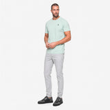 Man wearing a light green t-shirt and gray pants on a white background