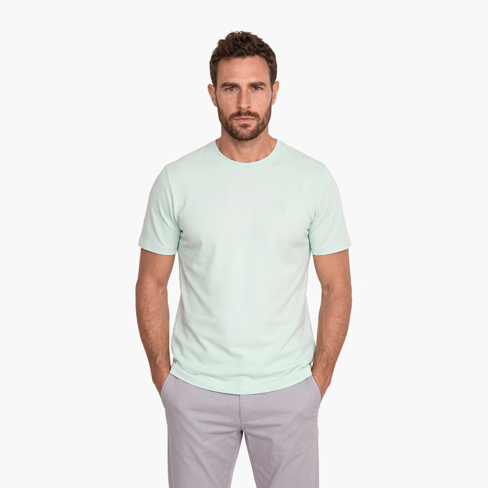 Man wearing a light green t-shirt and gray pants on a white background