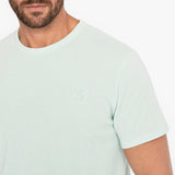 Man wearing a light green t-shirt with a small logo on a white background