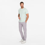 Man wearing a light green t-shirt and gray pants on a white background