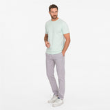 Man wearing a light green t-shirt and gray pants on a white background