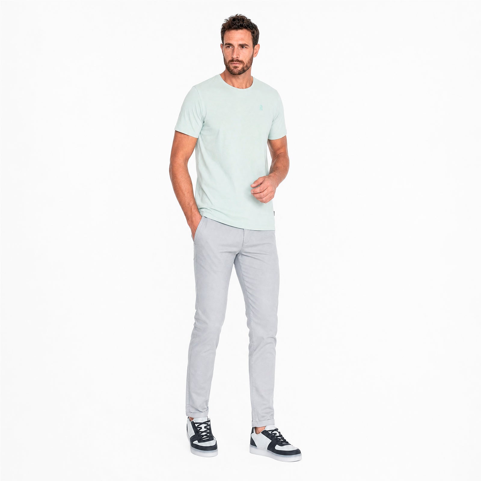 Man wearing a light green t-shirt and gray pants on a white background