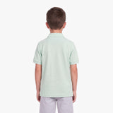A child viewed from the back, wearing a light mint green polo shirt and light gray pants