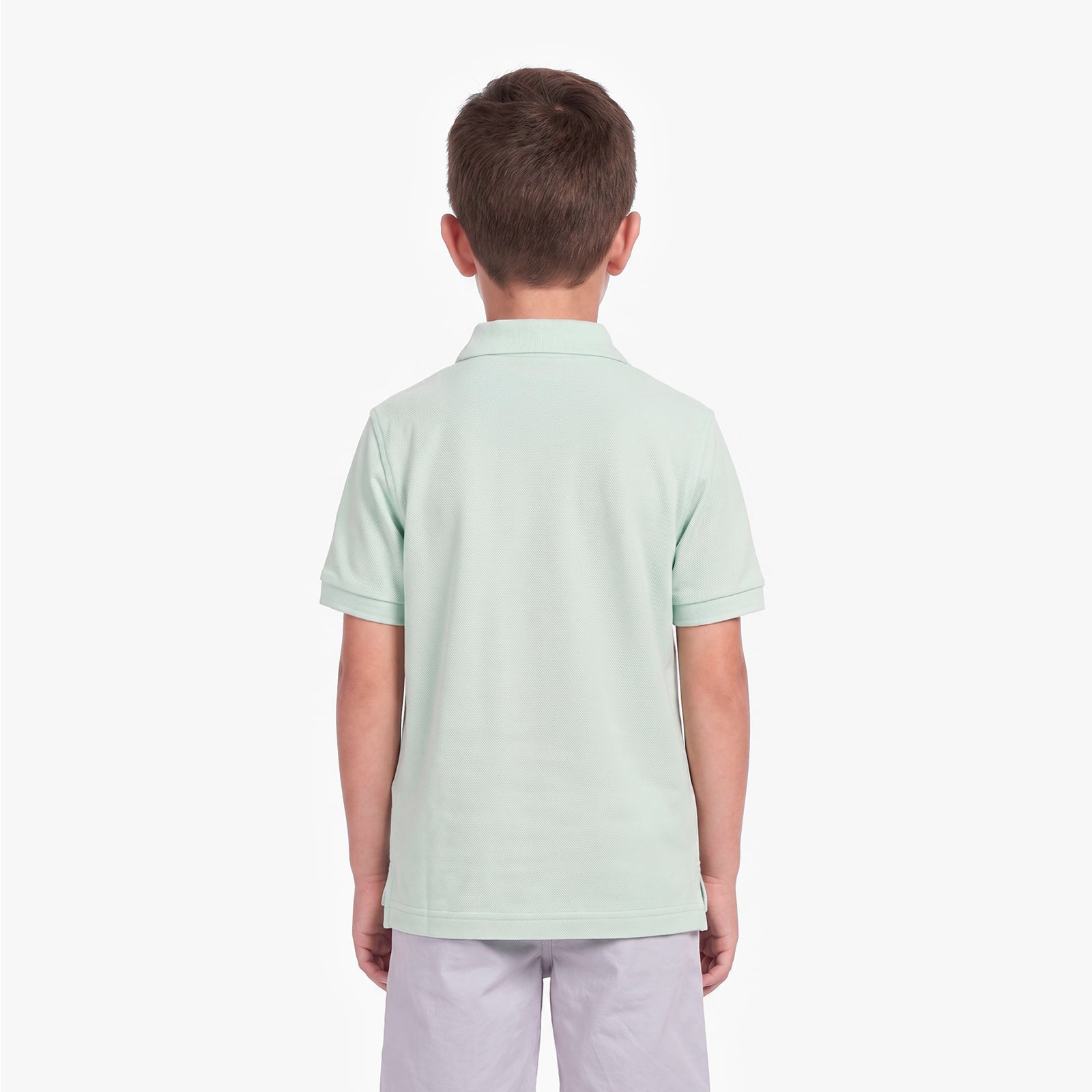A child viewed from the back, wearing a light mint green polo shirt and light gray pants
