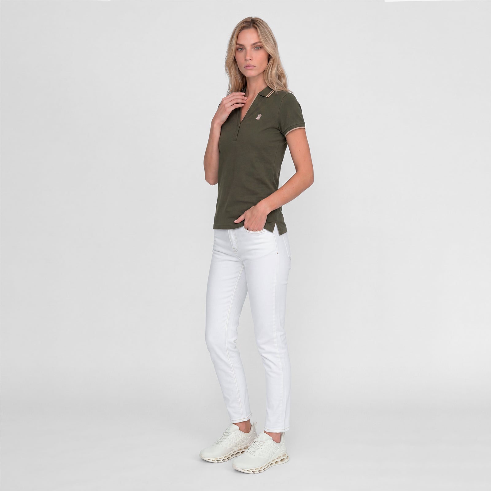 Woman wearing a green polo with an embroidered beige dog logo on a white background