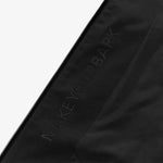 Close-up of a black fabric featuring the words 'MAKEYOURBARK' subtly printed in dark lettering along the side of a black zipper. The text blends into the fabric, maintaining a minimalist and sleek design.