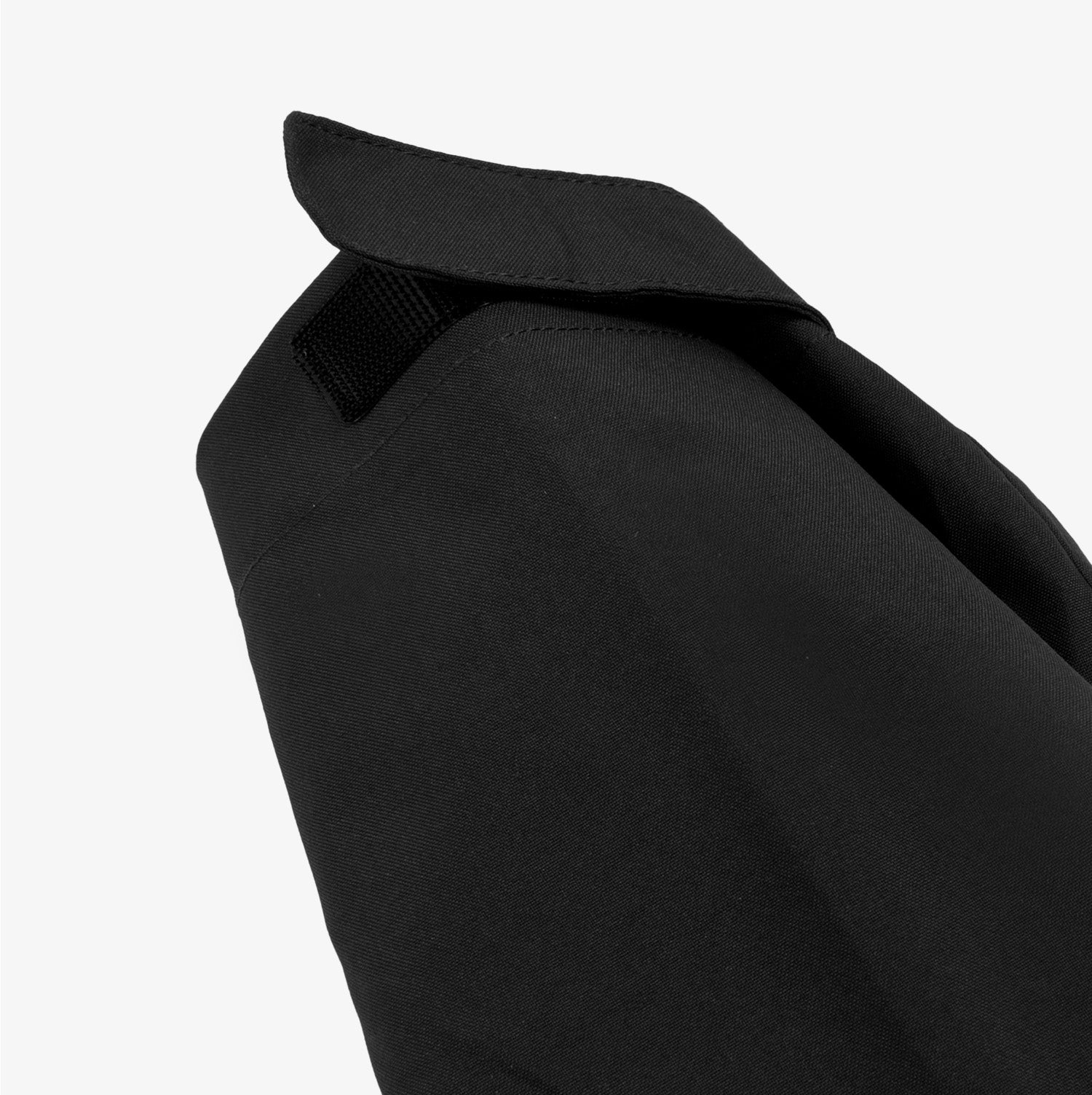 Close-up side view of the sleeve and shoulder area of a black jacket. The image highlights the clean stitching and the structured design of the shoulder. A small black strap detail is visible near the collar, adding functionality and style to the jacket.