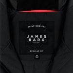 Close-up of the inside label of a black jacket. The black label features the text 'PRIVÉ SOCIETY' at the top, with 'JAMES BARK' prominently in the center, followed by 'EST. 2015.' Below, the label reads 'REGULAR FIT,' and a smaller tag beneath indicates the size 'M' and 'Made in China.' The design is minimal and clean, with a red accent visible in the lining.