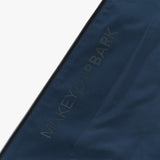 Close-up of a navy blue fabric featuring the words 'MAKEYOURBARK' printed in subtle, dark lettering along the side of a black zipper. The text blends smoothly with the fabric, maintaining a sleek and minimalist design.