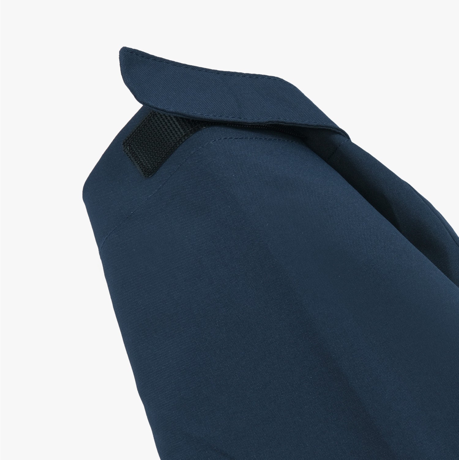 Close-up side view of the sleeve and shoulder area of a navy blue jacket. The image highlights the clean stitching and the structured design of the jacket's shoulder. A small black strap detail is visible near the collar, adding functionality and style to the jacket.