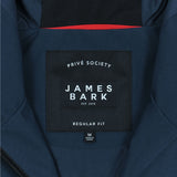 Close-up of the inside label of a navy blue jacket. The black label features the text 'PRIVÉ SOCIETY' at the top, with 'JAMES BARK' prominently in the center, followed by 'EST. 2015.' Below, the label reads 'REGULAR FIT,' and a smaller tag beneath indicates the size 'M' and 'Made in China.' The design is minimal and clean, with a red accent visible in the lining.